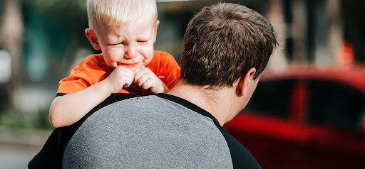 father carries toddler in arms as toddler about to cry KHM Attorneys at Law Colorado Springs, Castle Rock