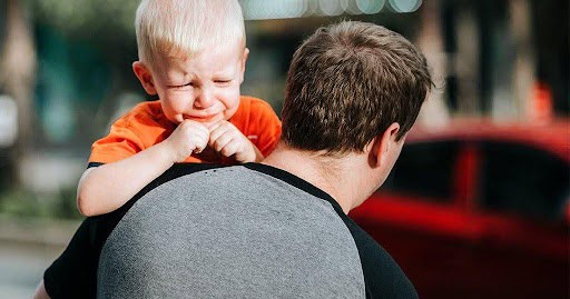 father carries toddler in arms as toddler about to cry KHM Attorneys at Law Colorado Springs, Castle Rock