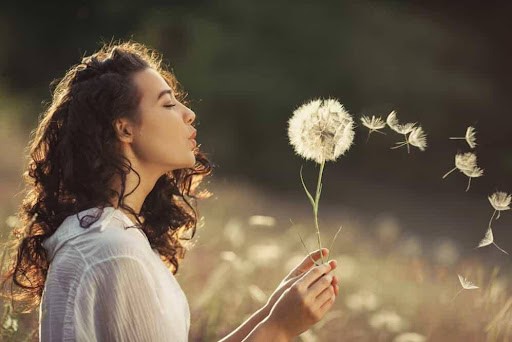 woman blows a large dandelion in a park, feeling independence KHM Attorneys at Law Colorado Springs, Castle Rock