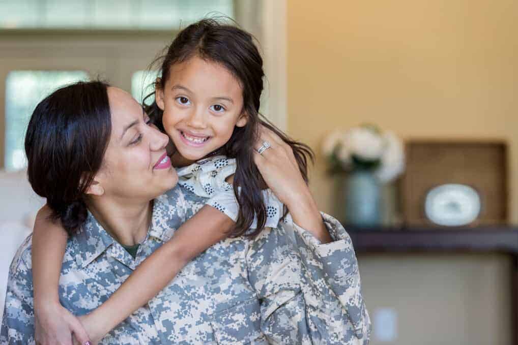 woman wearing military fatigues looks at daughter who is hugging her from her back KHM Attorneys at Law Colorado Springs, Castle Rock