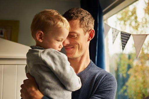 father smiles as he holds son in his arms while standing in backyard KHM Attorneys at Law Colorado Springs, Castle Rock