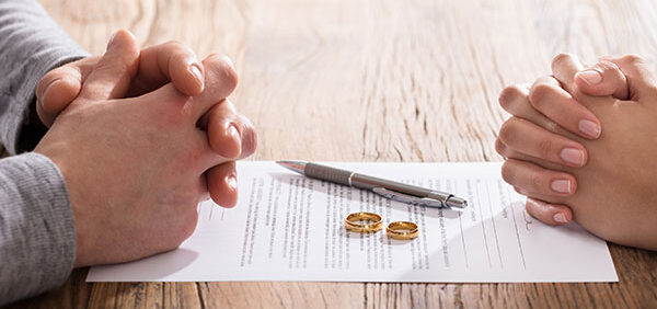 man and woman sit at table with fingers folded as they sign alimony paperwork KHM Attorneys at Law Colorado Springs, Castle Rock