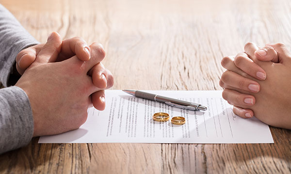 man and woman sit at table with fingers folded as they sign alimony paperwork KHM Attorneys at Law Colorado Springs, Castle Rock